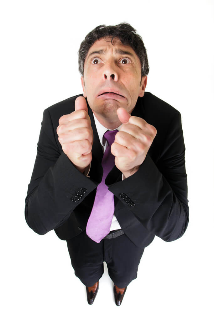 Comic high angle portrait of a middle-aged businessman with a scared fearful expression raising his fists to his face as though beseeching help, isolated on white
