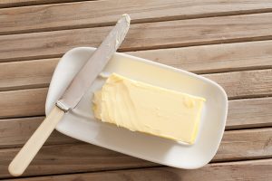 Pat of fresh farm butter on a butter dish with a knife to use as a spread or cooing ingredient overhead view on a slatted wooden table
